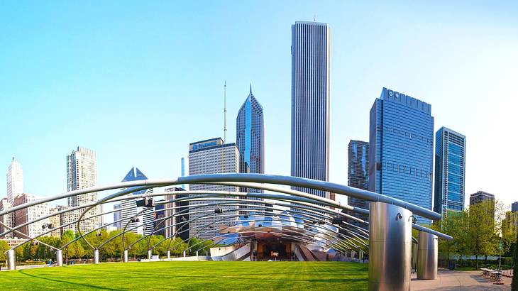 A park with grass that has a metal structure above it and a skyline in the background
