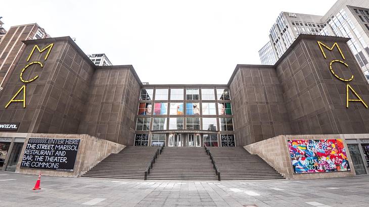 A museum building with steps leading up to it and yellow "MCA" signs on it