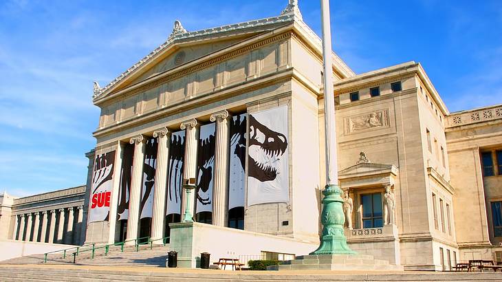 A Greek-style museum building with a banner with a dinosaur skeleton on it