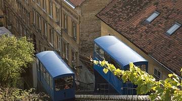 Two blue carts on a funicular amongst trees and buildings from above