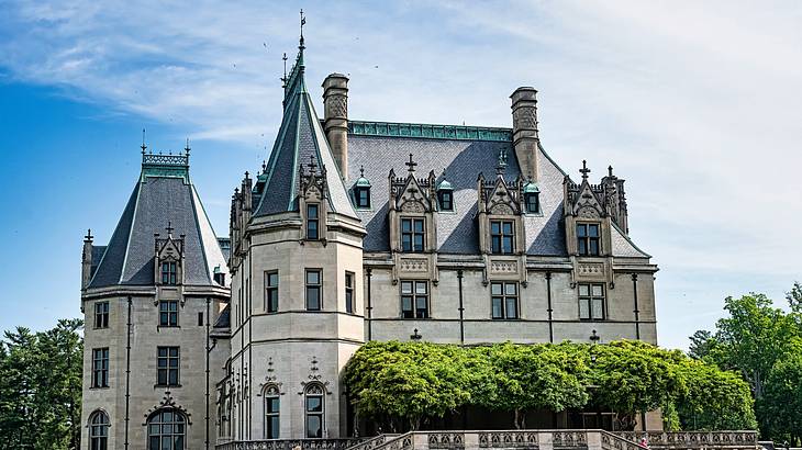 A mansion with ornate windows and blue roofs next to a green hedge