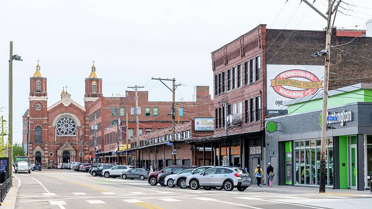 A street with cars, buildings, and a brick cathedral with two towers at the end