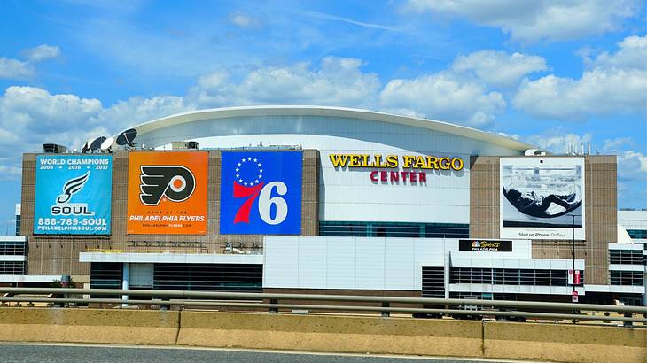 A facade of a building with sports team logos and a sign saying "Wells Fargo Center"