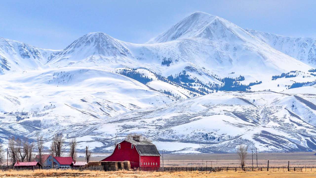 A small red barn next to snow-covered mountains under an icy blue sky