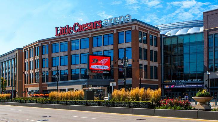 A building with many windows and a " Little Caesars Arena" sign next to a road