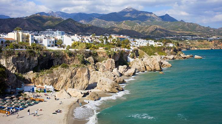 View of a beach with people, blue water and houses on cliffs, Costa del Sol, Spain