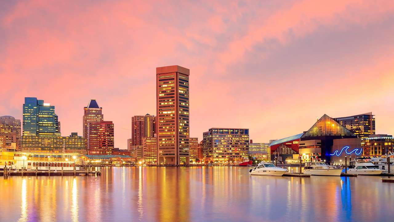 An illuminated city skyline next to the water at sunset under a pink sky
