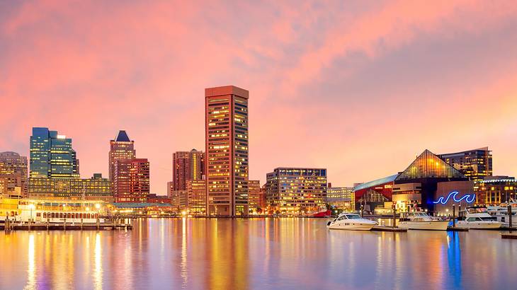 An illuminated city skyline next to the water at sunset under a pink sky