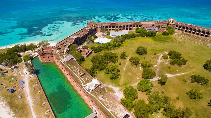 Aerial of a fortified park with green grass and trees surrounded by blue water