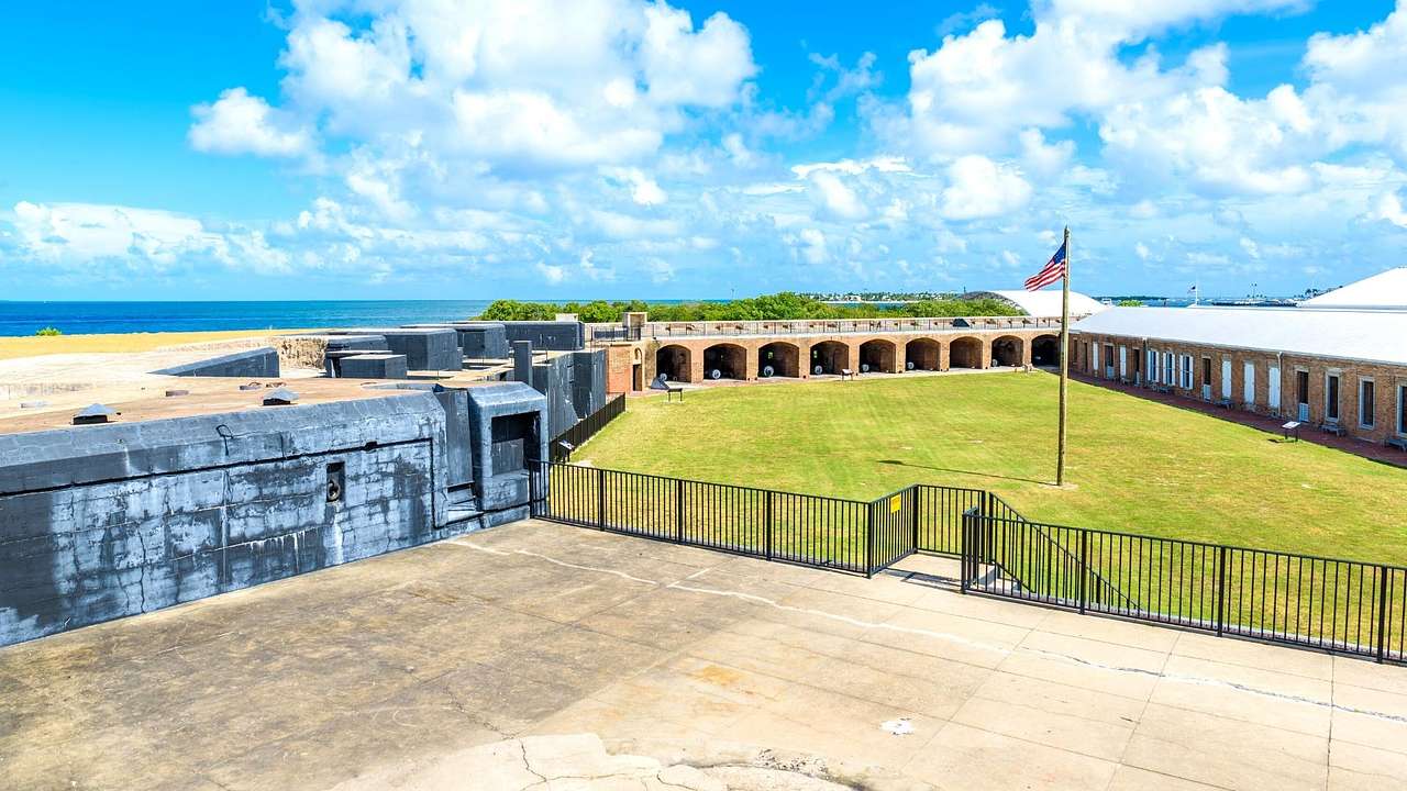 A park with green grass and an American flag, surrounded by fortified arched walls