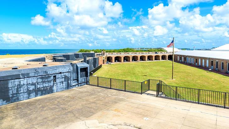 A park with green grass and an American flag, surrounded by fortified arched walls