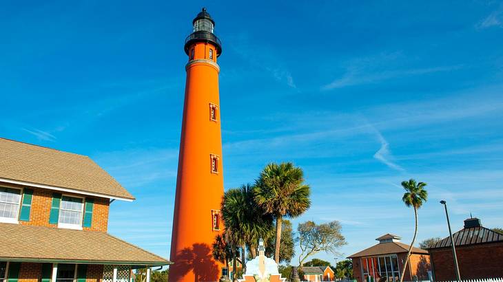 An orange lighthouse with houses and blue sky around