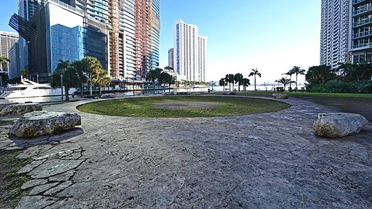 Grey pavement ground with a round grass patch against buildings