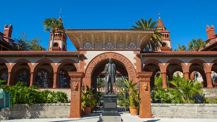 A statue of a man against a brown arched entrance with the text "Flagler College"