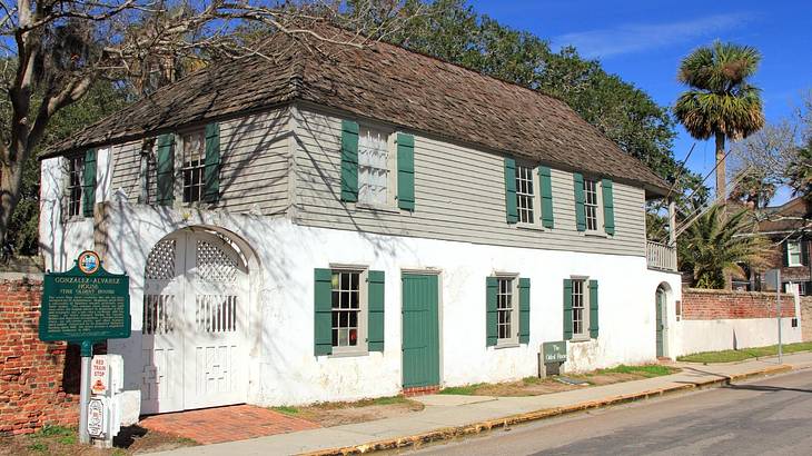 A vernacular white house with green door and windows and a dark brown roof