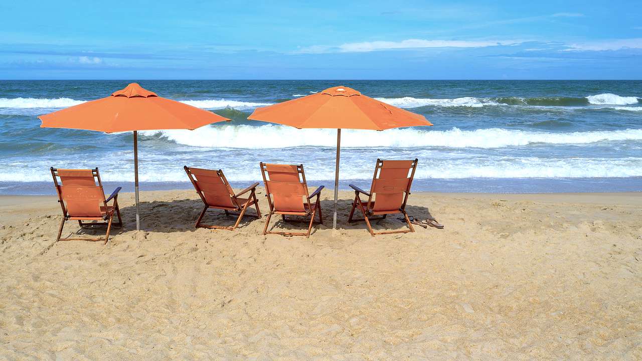 Two yellow beach umbrellas and deck chairs facing waves crashing onto the sandy beach