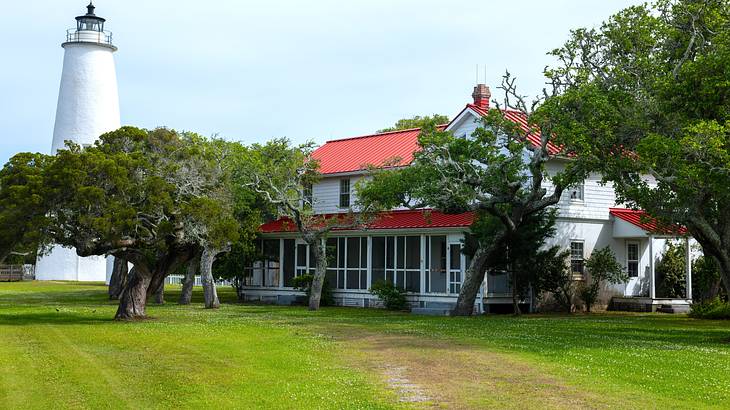 White lighthouse surrounded by green trees and a hidden red and white building