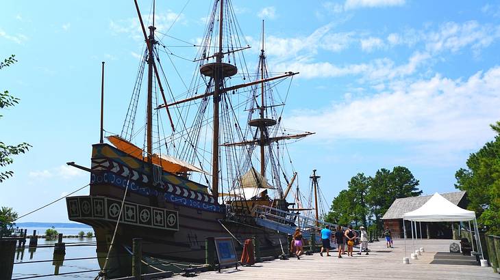 A historical ship docked on the water by a boardwalk under a partly cloudy sky