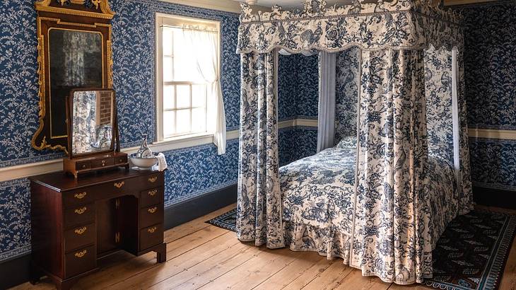 A four-poster bed and bed chamber in a room with a dressing table and a window