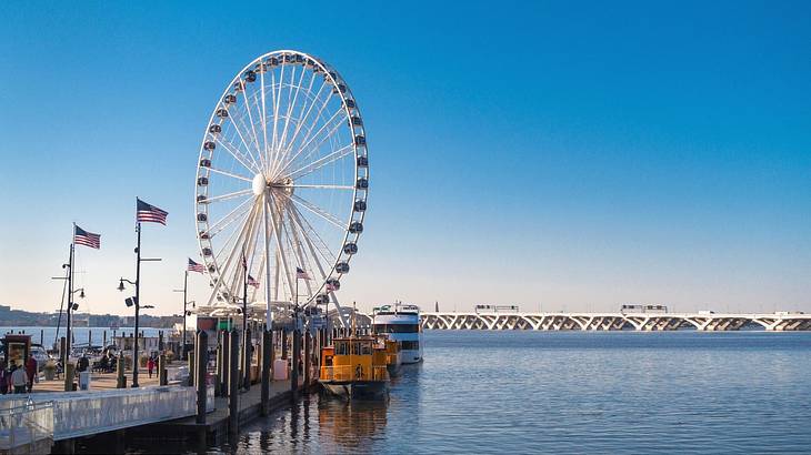 A Ferris wheel on a pier next to water under a blue sky