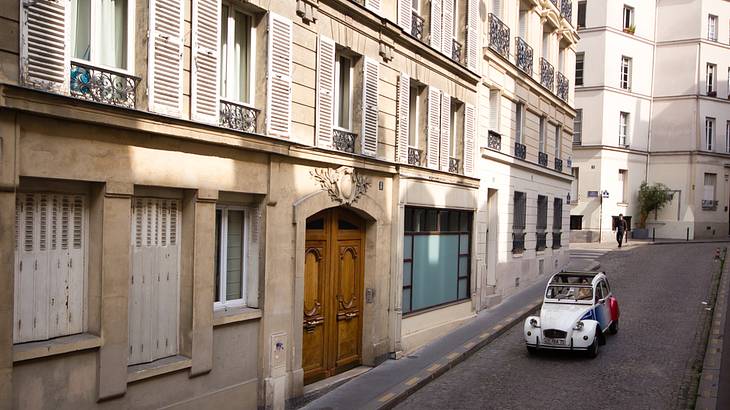 A French car being driven on a street lined with old buildings