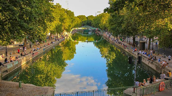 A canal surrounded by trees with people sitting along its edges