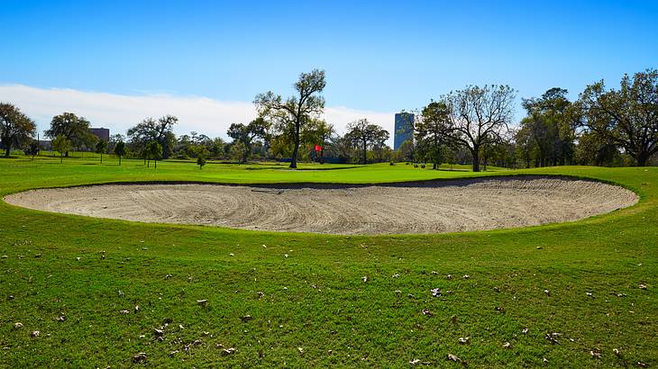 A bunker in a golf course bordered by trees under a blue sky