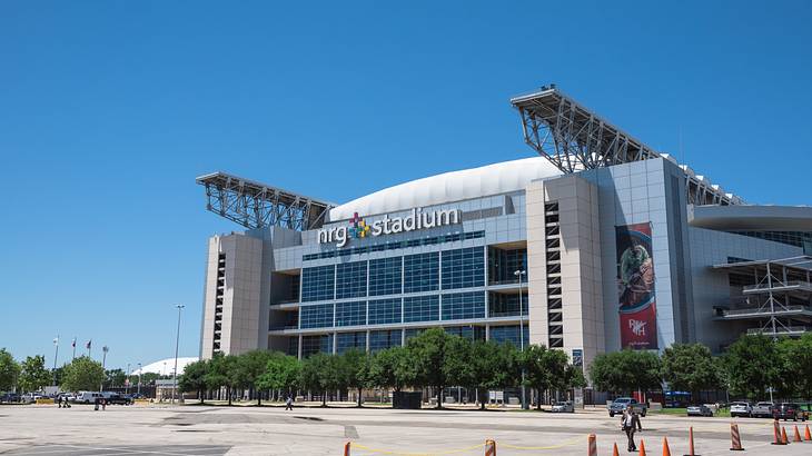 A facade of a large stadium with trees and an empty parking lot in front