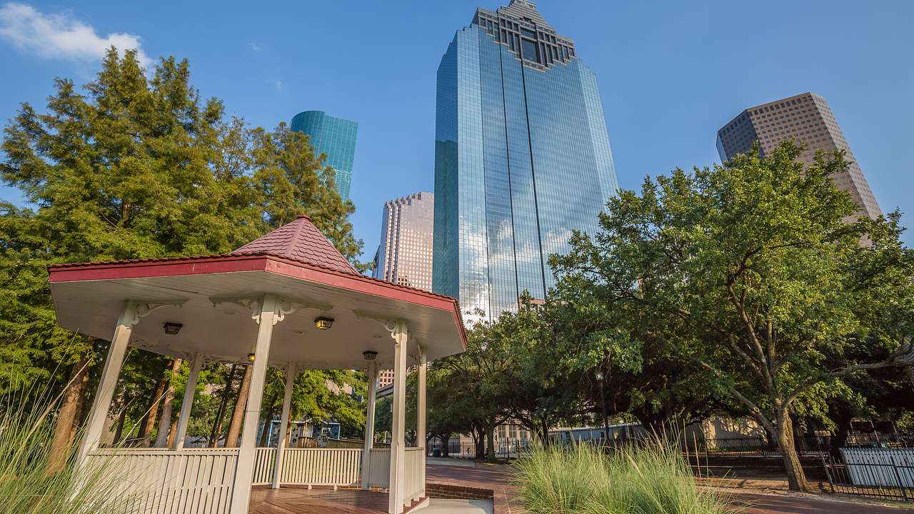 A gazebo next to trees and skyscrapers under a blue sky