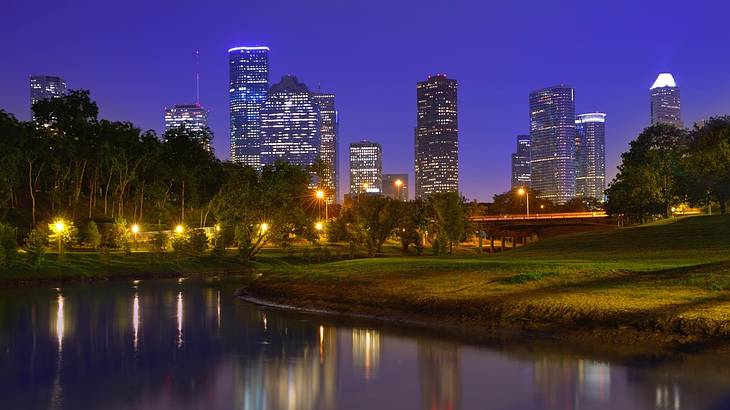 An illuminated skyline with a park and pond in the foreground