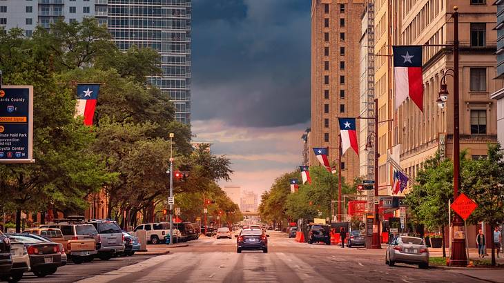 A street as the sun sets with cars, buildings, and Texas flags