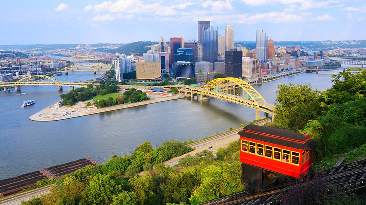 A red inclined tram with a river, a yellow bridge, and a city skyline below it