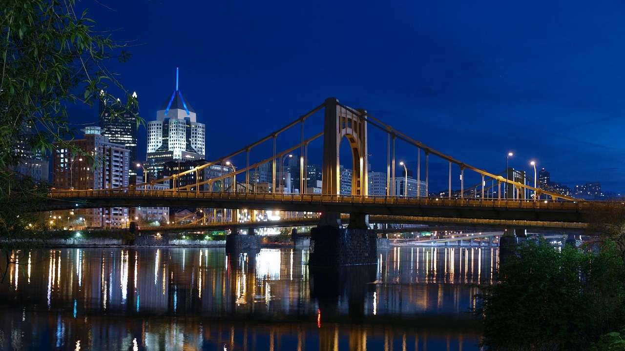 A bridge at night with buildings behind and lights reflecting on water