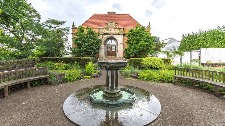 An old-fashioned manor house with a path, trees, and a fountain in front