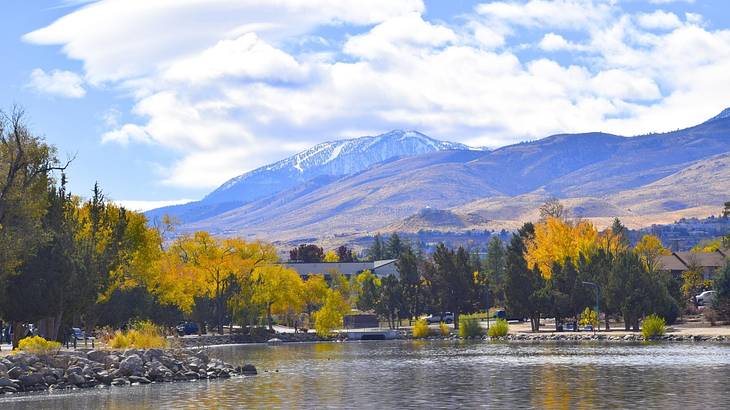 A lake next to mountains and trees under a blue sky with white clouds