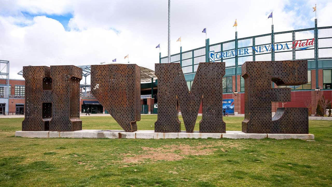 An iron sign that says "home" next to a stadium with a "Greater Nevada Field" sign