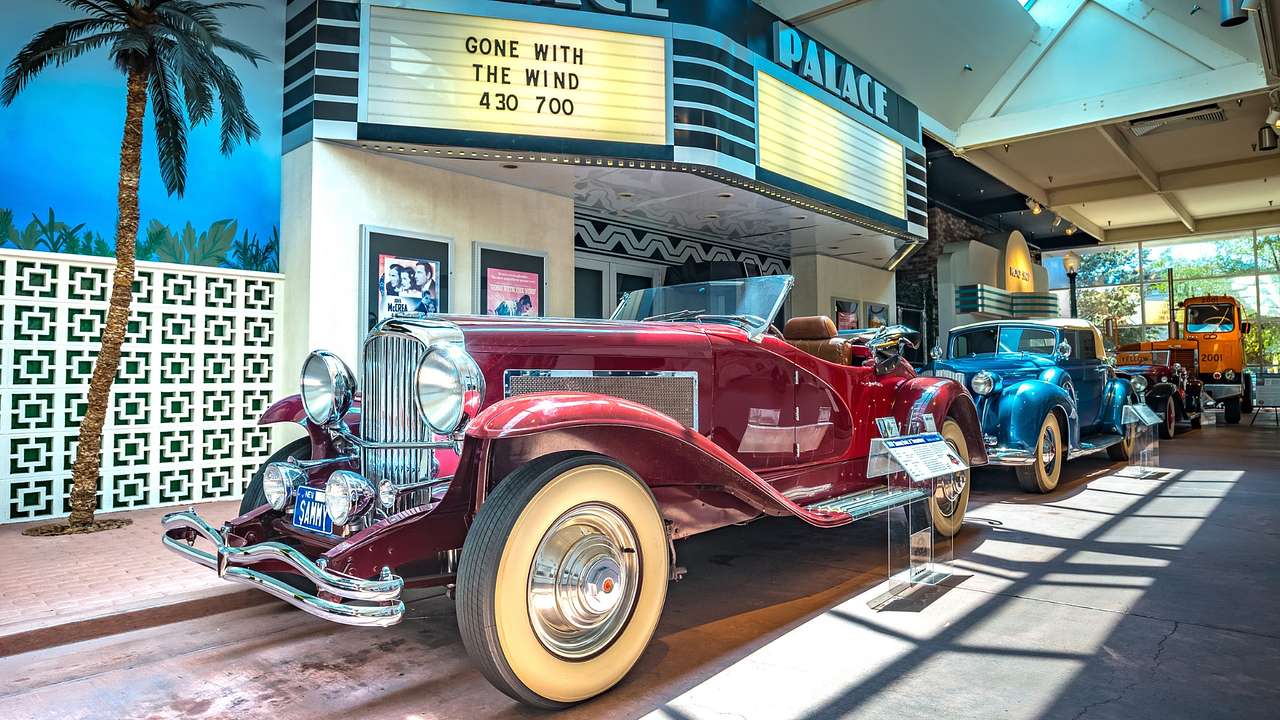 Old-fashioned cars in a museum next to a movie theater exhibit and a palm tree