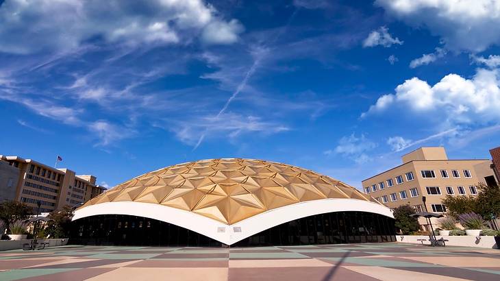 A modern gold dome-type structure next to a path under a blue sky with white clouds