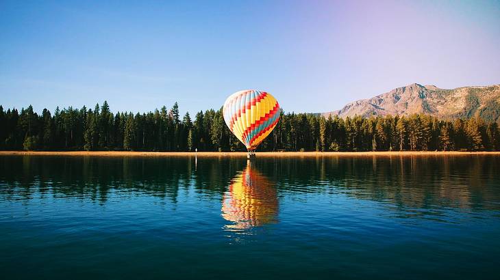 A colorful hot air balloon next to a lake and trees