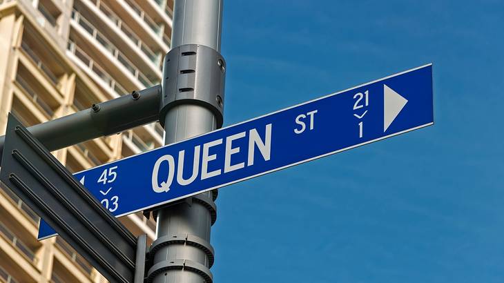 View of the Queen Street sign from below against a building and the blue sky