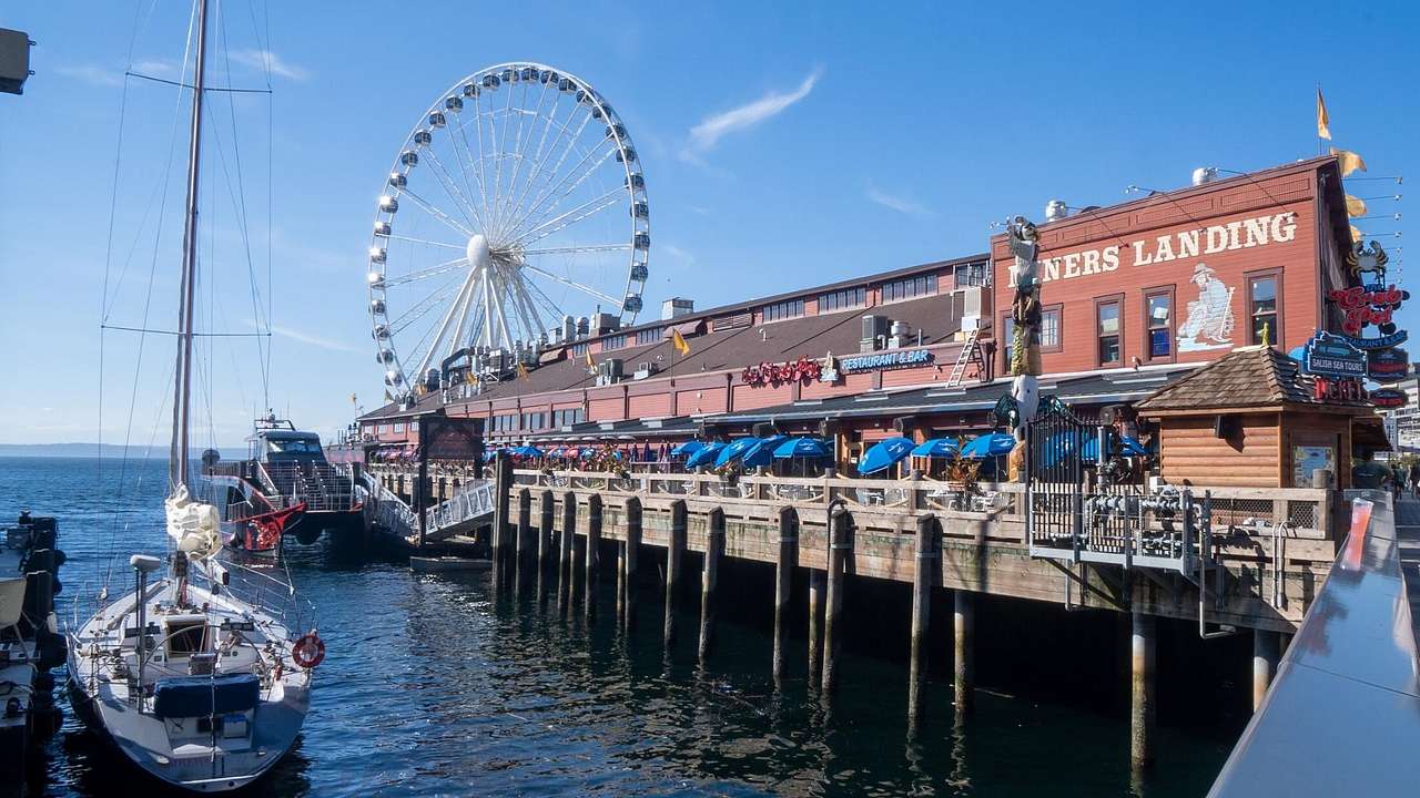 A pier front with a boat in the water, a building, and a Ferris wheel