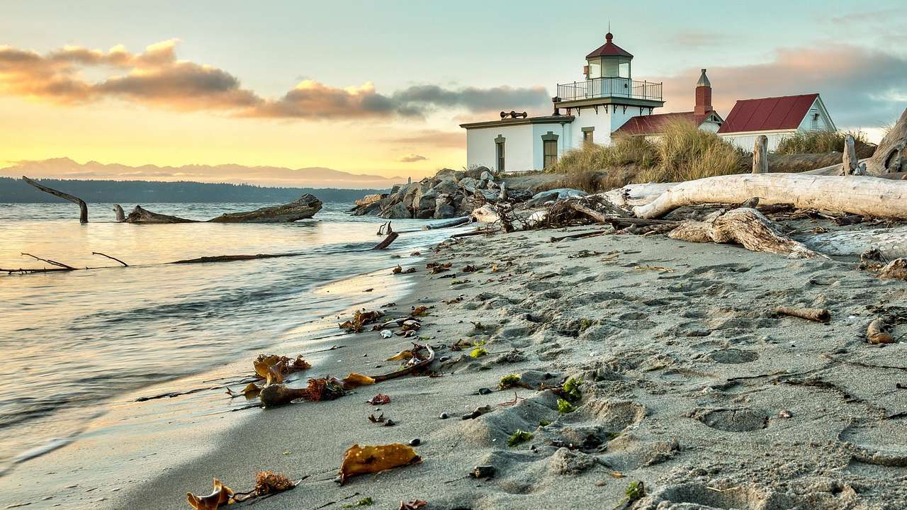 A lighthouse building with a sandy shore and ocean around it at sunset
