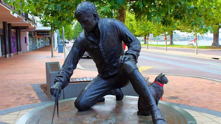 A statue of a man drawing with a compass with a cat next to him