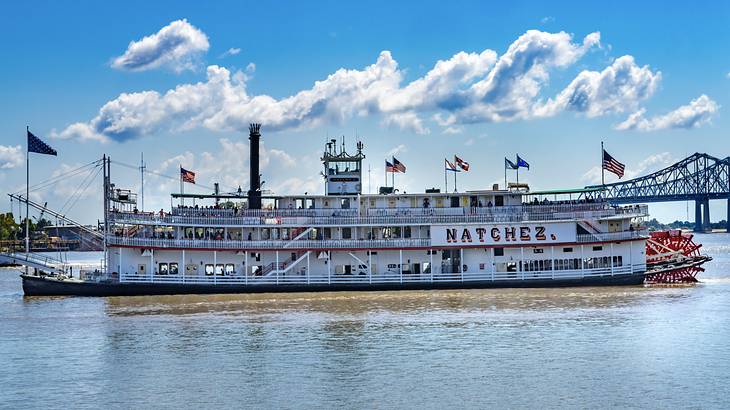 A cruise ship-style boat with flags on the water with a bridge behind