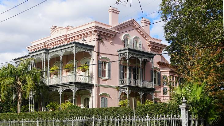 A large pink house surrounded by trees and an iron fence