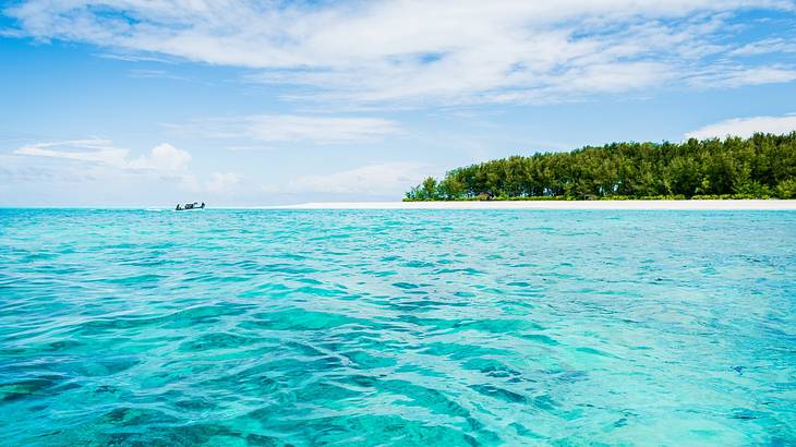 Sparkling blue ocean water next to an island with white sand and green trees