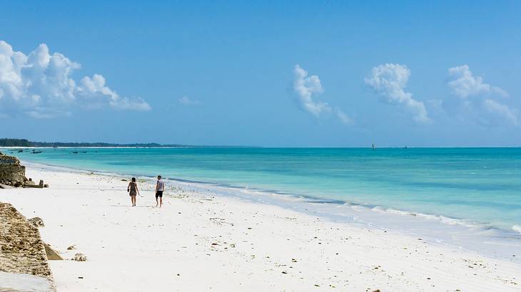 A white sand beach with two people on it next to turquoise ocean under a blue sky