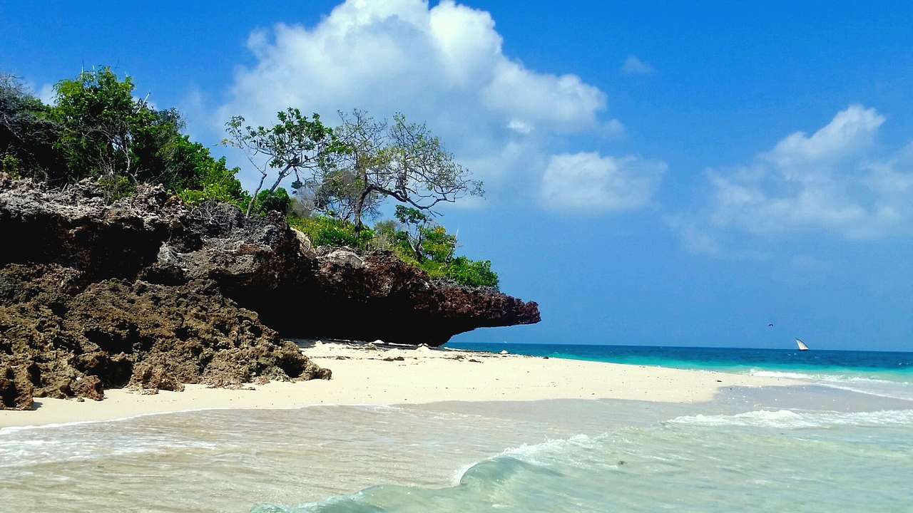 A white sand beach next to the ocean and rocks with green trees on them