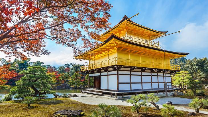 A yellow and white temple near many trees and a pond in the background