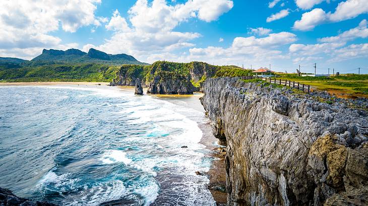 A long extending cliff near a body of water under a blue sky with clouds